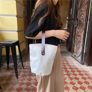 Detail of white canvas tote bag featuring a smile face and brown leather handles