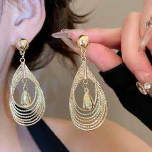 Macro shot of layered gold teardrop earrings with intricate woven metal texture details