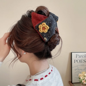 Detail shot of a large plush bow hair claw clip worn on a bun hairstyle with knit flower accent