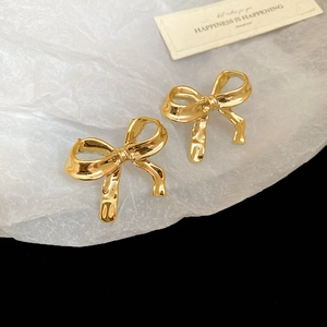 Détail de boucles d'oreilles nœud doré avec fini métallique brillant sur papier blanc