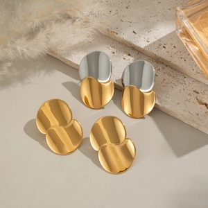 Close-up of geometric two-tone gold and silver circular stud earrings with metallic mirror finish