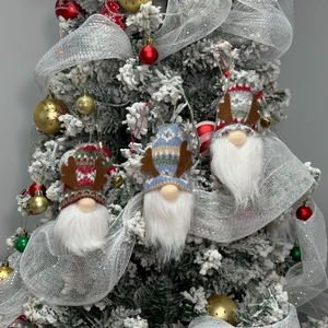 Three plush Christmas gnomes with knit hats and reindeer antlers on a snowy tree