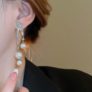 Détail macro de boucles d'oreilles argentées avec strass pavés et trois perles blanches