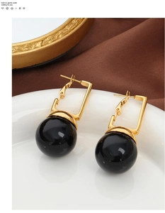 Gros plan de boucles d'oreilles géométriques dorées avec de grandes perles noires polies