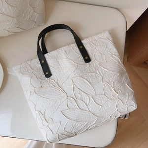 Macro detail of leaf embroidery on off-white canvas tote with black leather handle