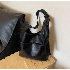 Detail der schwarzen Leder-Beuteltasche mit Ziernaht und verstellbarem Riemen auf Steinsockel