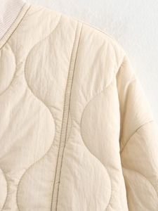 Close-up of beige quilted jacket featuring wave stitching patterns and ribbed collar detail