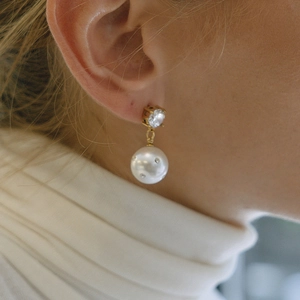 Detailaufnahme der Titan-Perlenohrringe mit Diamantinlay an einem Model in weißer Kleidung
