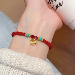 Détail du bracelet en perles d'agate rouge avec un charm cadenas doré au poignet