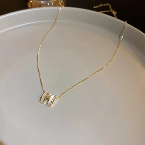 Close-up of gold-plated H-letter necklace with white shell inlay on a grey jewelry tray