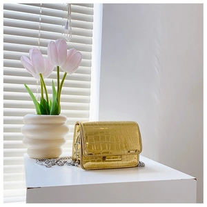 Detail of gold crocodile embossed crossbody bag with metal chain on a white platform