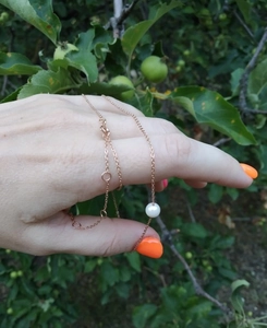 Detail showing elegant rose gold necklace with a single white pearl held in hand outdoors