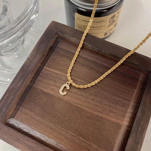 Gros plan sur une chaîne torsadée dorée avec un pendentif lettre C serti de cristaux