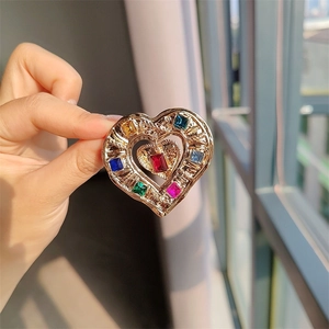 Detail of a vintage gold heart brooch with colorful square crystals held in hand