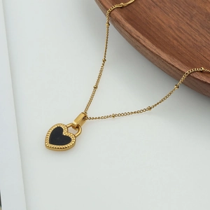 Close-up of gold 18K titanium steel heart pendant with black inlay on wooden tray