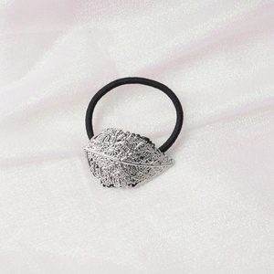 Detail of a silver leaf-shaped metal charm on a black elastic hair tie over white silk