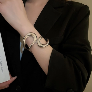 Close-up of polished silver geometric open cuff bracelet on female wrist with black suit