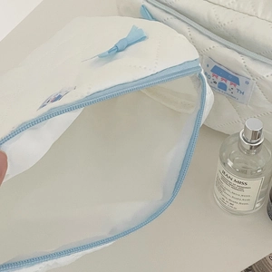 Detail of white quilted cosmetic bag featuring light blue bow and branded cloth label