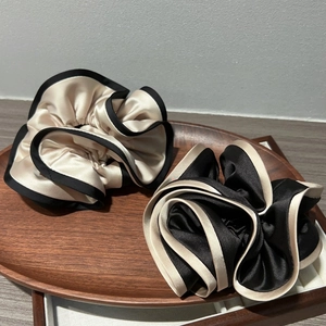 Close-up of elegant double-layered satin scrunchies in beige and black on a wooden tray
