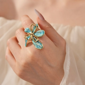 Close-up of a vintage teal enamel flower ring with gold edges on a model's finger
