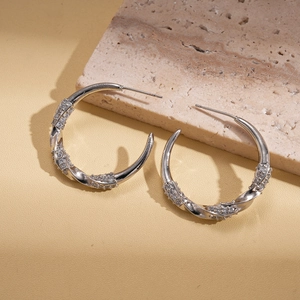 Dettaglio di orecchini a cerchio ritorti in argento con zirconi incastonati su pelle beige