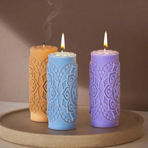 Three lit mandala relief pillar candles in orange, blue, and purple on a stone tray