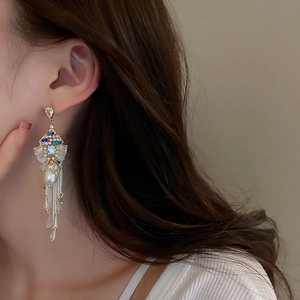 Close-up of long tassel earrings with colored zircons and pearls on model ear
