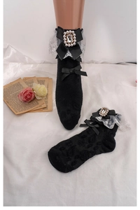 Detail of black Lolita socks with white lace, black bows, pearls and sparkling rhinestones
