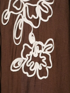 Close-up of white rope embroidery on dark brown textured fabric of a floral shirt