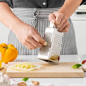Multifunctional 4-sided stainless steel kitchen grater grating garlic in a kitchen setting
