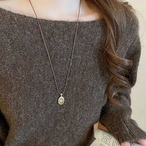 Detailed close-up of golden spiral texture pendant on a long brown wax cord necklace