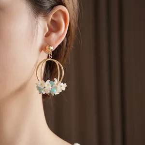 Elegant gold hoop earrings with white flowers and light blue beads worn by a model