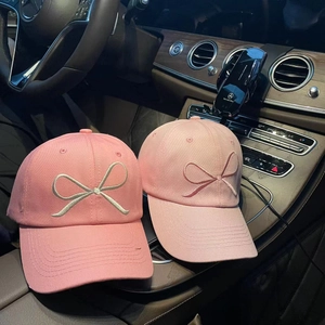 Pink baseball caps with bow embroidery on a car dashboard under natural light