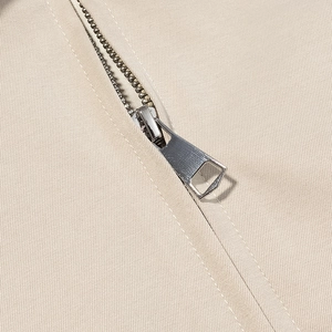 Close-up of a high-quality silver metal zipper on beige twill fabric garment detail