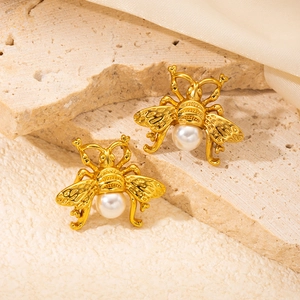 Macro shot of gold vintage bee earrings with pearls on textured stone and silk fabrics