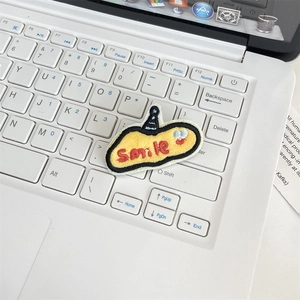 Close-up of yellow oval embroidered patch with Smile text on a white laptop keyboard