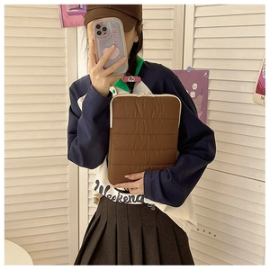 Detail of dark brown quilted laptop sleeve with stitch texture held by a model