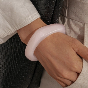 Macro detail of a wide semi-transparent resin bangle in soft pink on a model's wrist