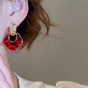 Detail of red geometric acrylic pendant earring with gold textured metal finish