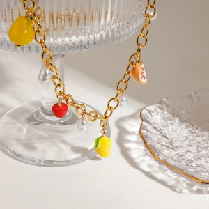 Gold stainless steel necklace with enamel fruit charms and white pearls on a glass stand