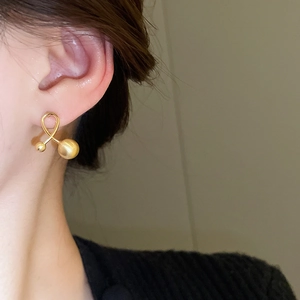Close-up of elegant gold-plated crisscross ball stud earring on model's ear