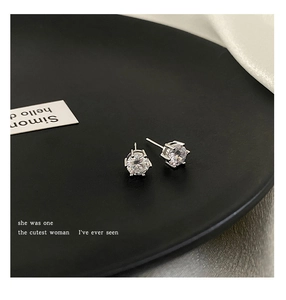 Macro detail of silver round zircon studs with four-prong setting on a black plate