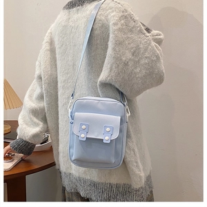 Close-up of light blue canvas crossbody bag with white buttons and adjustable strap