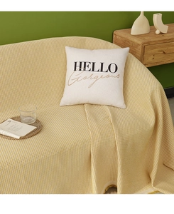 Detail of waffle weave yellow throw blanket with tassels and beige graphic pillow