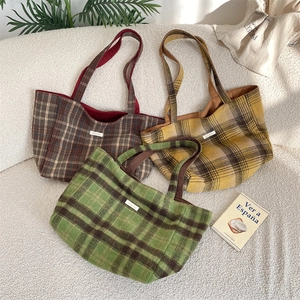Three oversized plaid tote bags in green, yellow, and red on a cozy fleece sofa