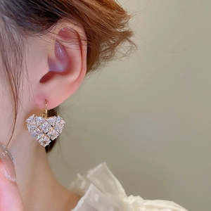 Detailed close-up of golden heart-shaped zircon earrings worn on a woman's ear