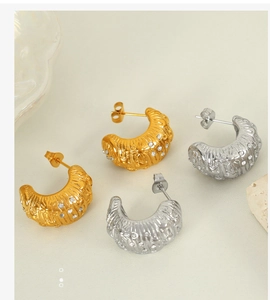 Detail of C-shaped gold and silver earrings with wave texture and rhinestone inlay
