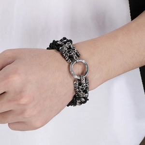 Close-up of a men's braided leather bracelet featuring vintage silver skull charms