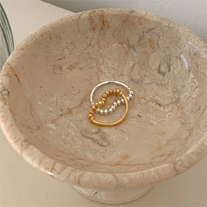Detail of interlocking gold and silver beaded rings on a marble tray background
