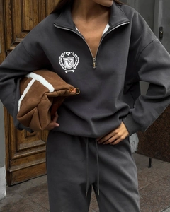 Détail d'un ensemble de survêtement gris foncé avec demi-zip, logo blanc et pantalon à cordon